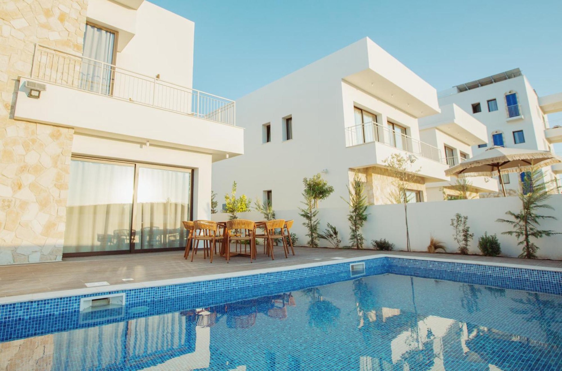 וילת בוטיק לבנה של Resortis באורוקליני בשעת זהב, עם בריכת פסיפס כחולה, פינת אוכל מראטן ושמשייה